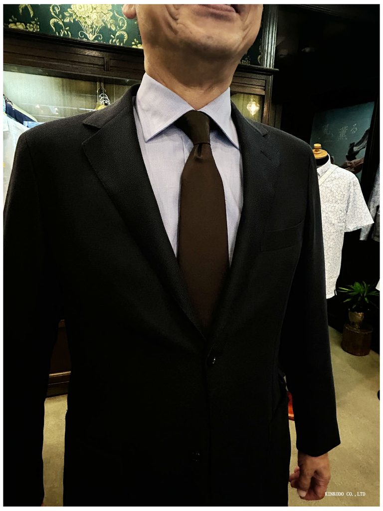 Tシャツの胸元、ネイビージャケットにブルーのトーマスメイソンのオーダーシャツそしてブラウンのソリッドタイ
